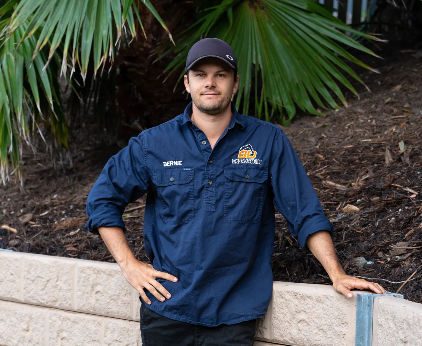 Bernie, qualified land surveyor at BD Excavation Services, standing beside a completed retaining wall